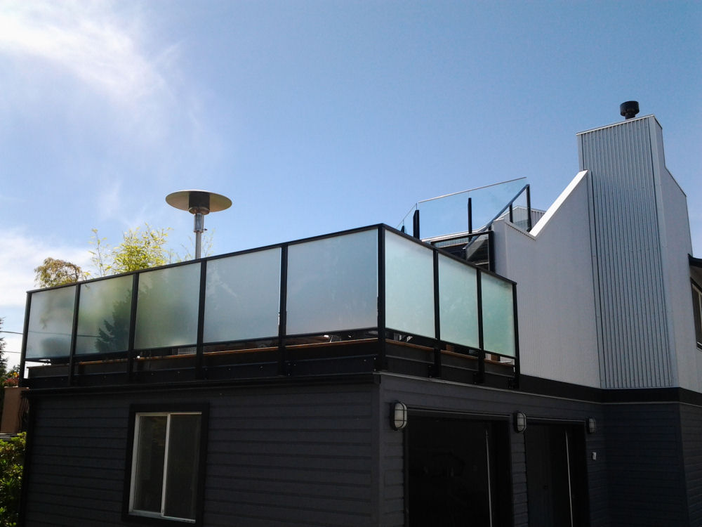 Modern two-story house exterior with a glass-paneled rooftop patio, gray siding, and white chimney