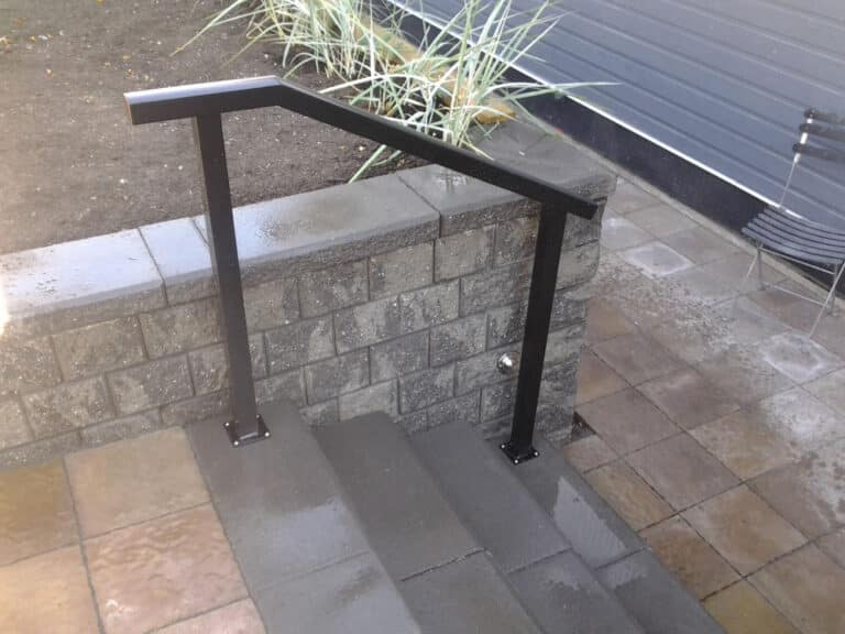 A black metal handrail is installed along concrete steps next to a cinder block retaining wall, with