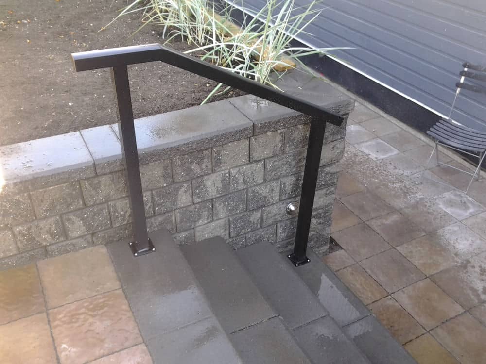 A black metal handrail is installed along concrete steps next to a cinder block retaining wall, with