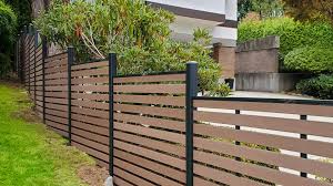 Modern horizontal wooden fence with black vertical posts, bordering a garden with green plants and