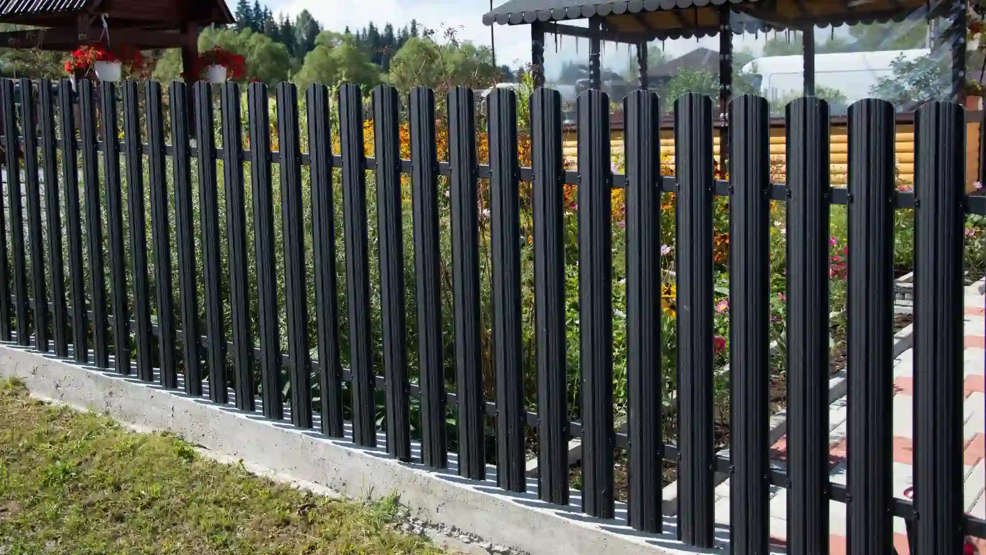 A tall black metal fence with vertical slats stands on a concrete base, featuring sturdy metal