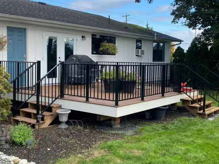 A raised wooden deck with sleek metal railings, steps on each side, a grill, and potted plants