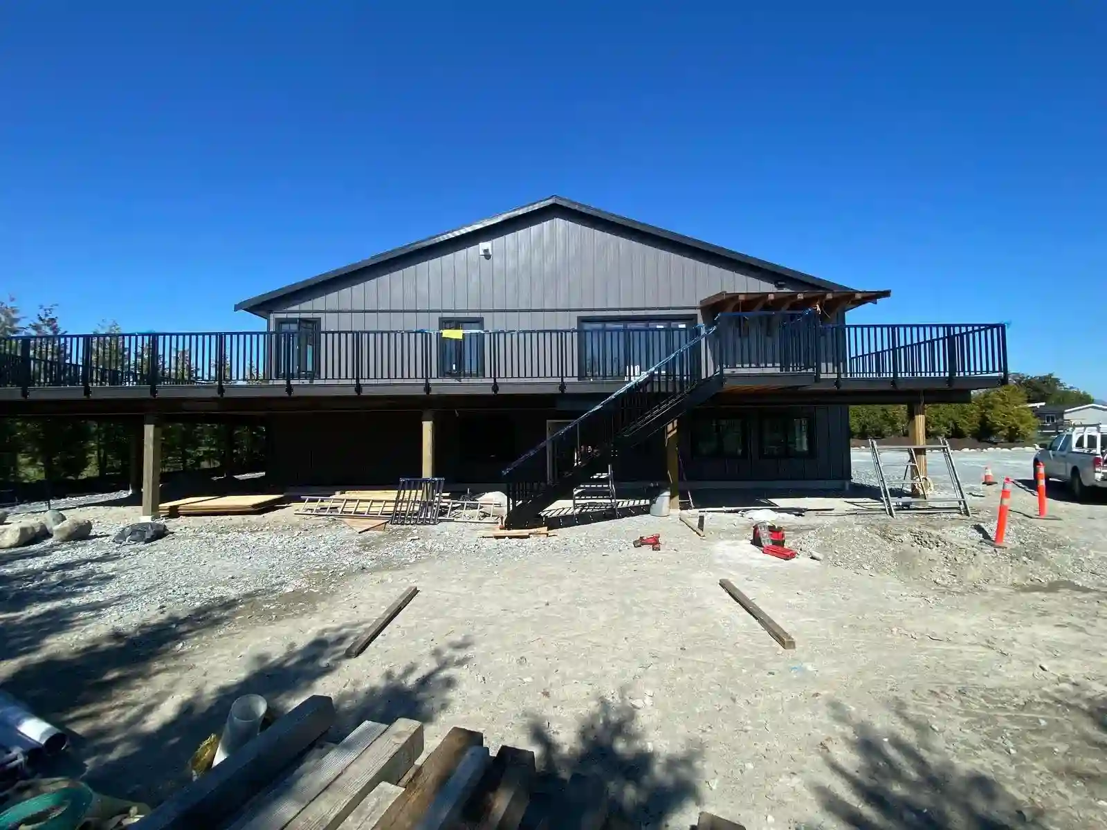 A gray two-story building with metal railings on its elevated deck and exterior stairs is under