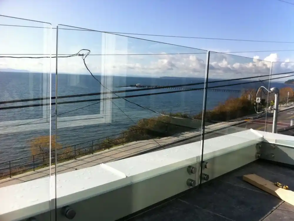 A glass balcony railing by LDH Aluminum Ltd. – Railings & Gates overlooks the ocean, a pier, and