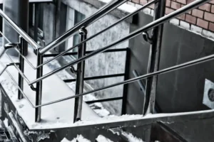 Snow-covered outdoor concrete steps with sturdy aluminum railings installed on stairs, next to a