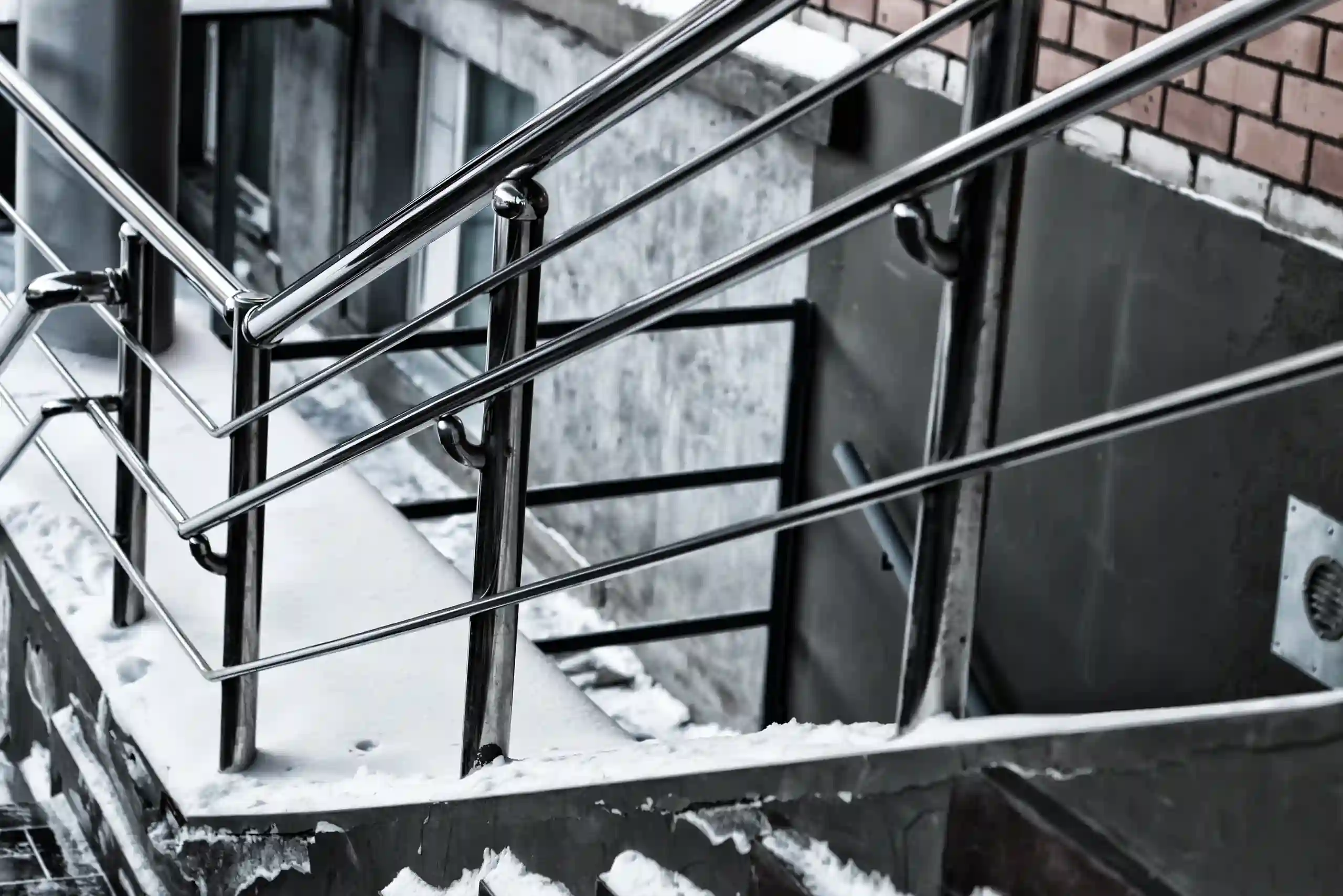 Snow-covered outdoor concrete steps with sturdy aluminum railings installed on stairs, next to a