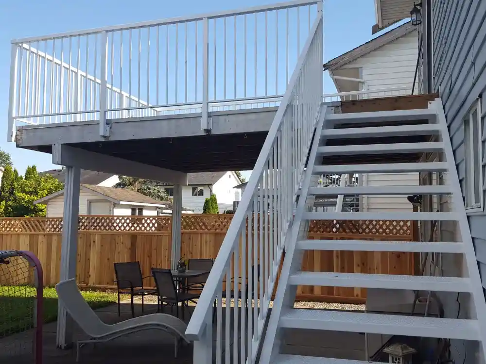 White wooden stairs lead to an elevated deck with a white railing; a table and chairs are beneath
