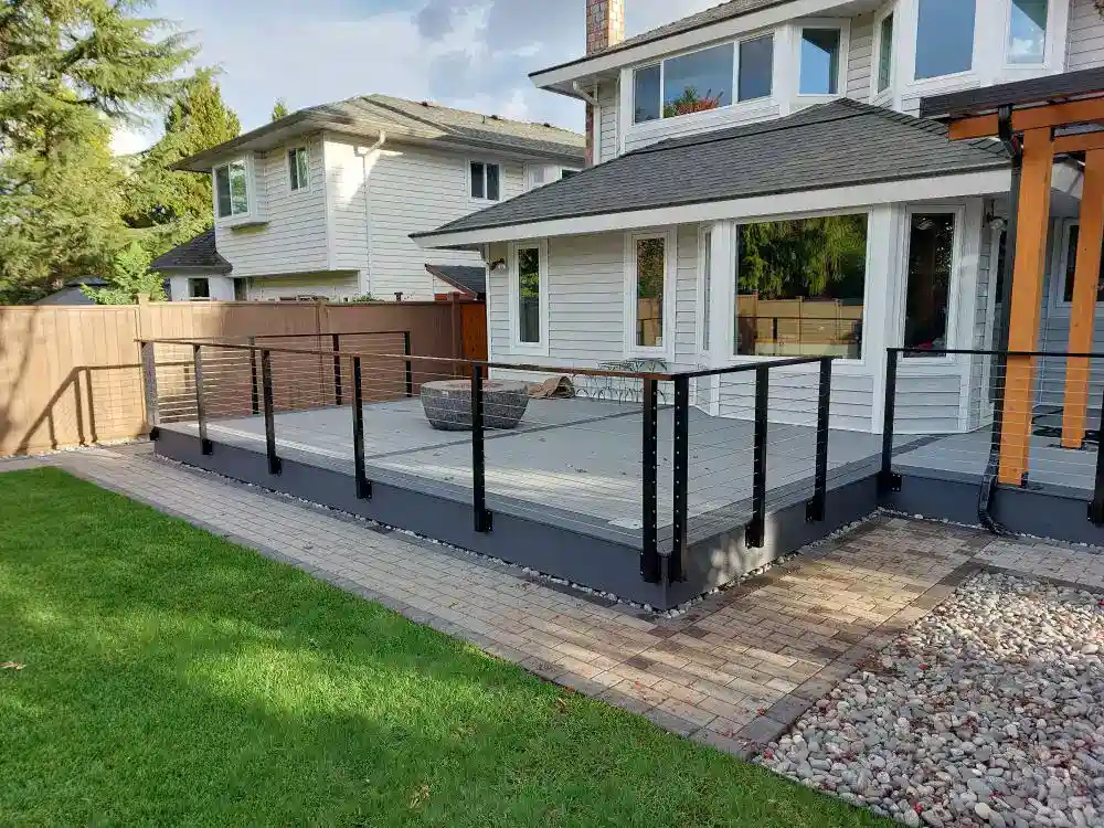 Modern backyard deck with black cable railing and custom aluminum railings, bordered by stone pavers