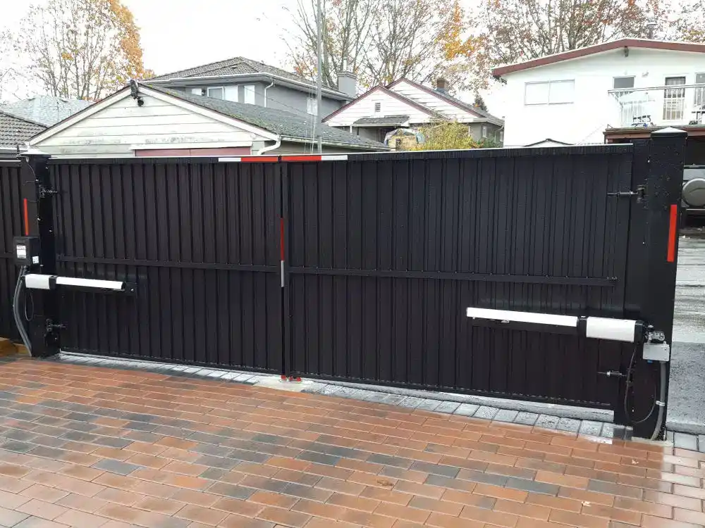 A black metal automatic sliding gate is closed across a driveway with brick paving, elegantly