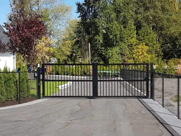 A sturdy black metal driveway gate blocks a paved entrance, acting as one of the main gates to the