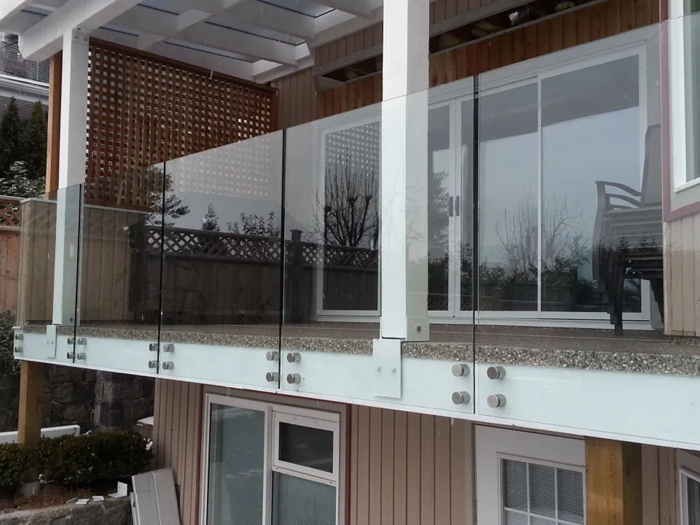 A modern house patio with a clear glass balcony railing, white pillars, and sliding glass doors