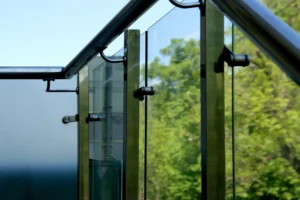 Close-up view of glass panels and metal supports on a structure with trees and blue sky visible in