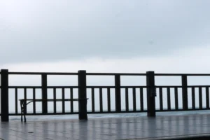 Wooden deck with aluminum railings overlooks a misty, overcast horizon. A bench sits on the left