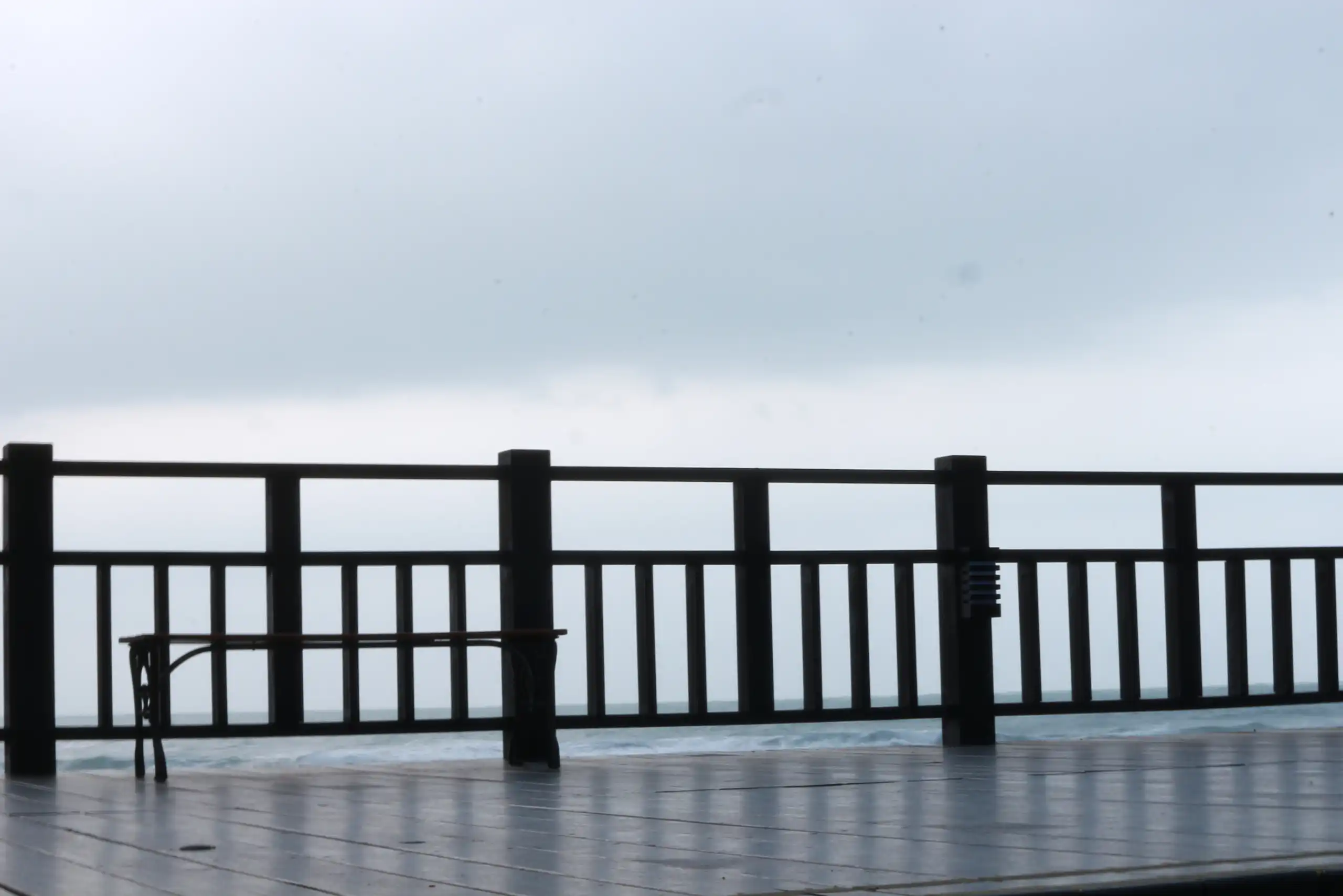 Wooden deck with aluminum railings overlooks a misty, overcast horizon. A bench sits on the left
