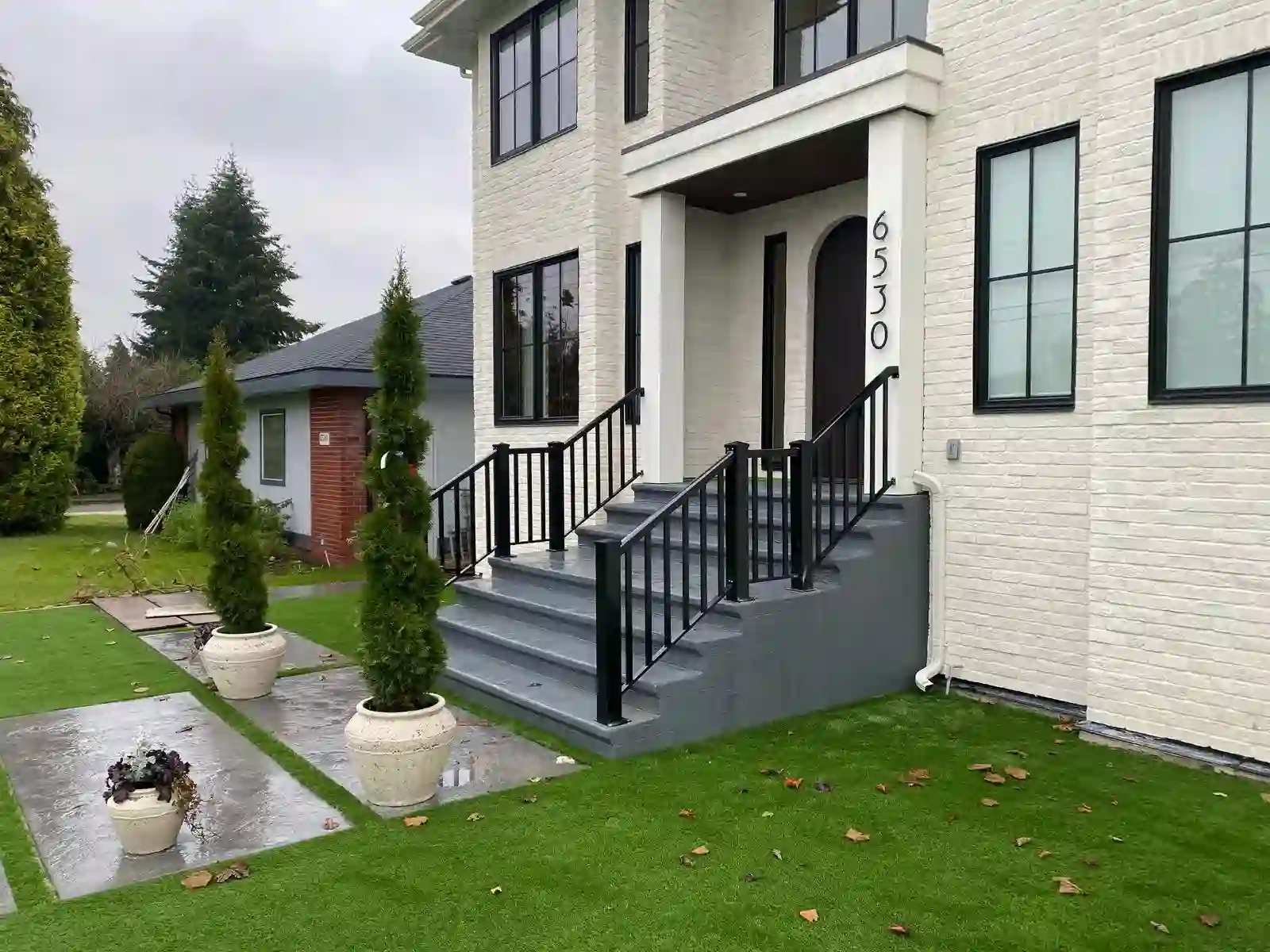 A modern two-story house with a white brick exterior, black trim, and gray stairs featuring sleek