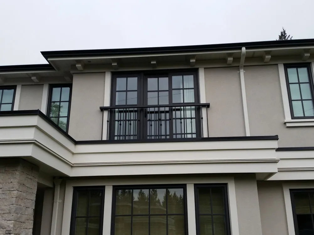 Second story of a modern house with gray walls, black framed windows, a small balcony with metal