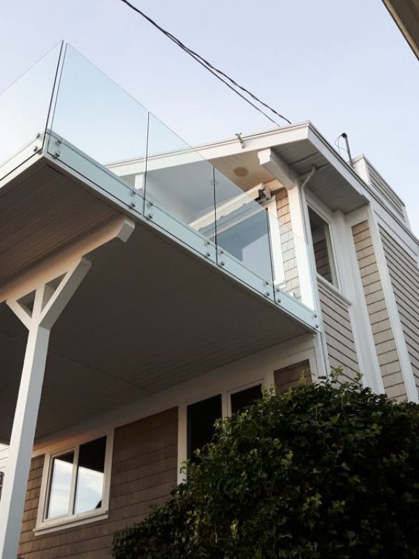 Exterior view of a modern two-story house with a glass balcony and beige siding, taken from a low